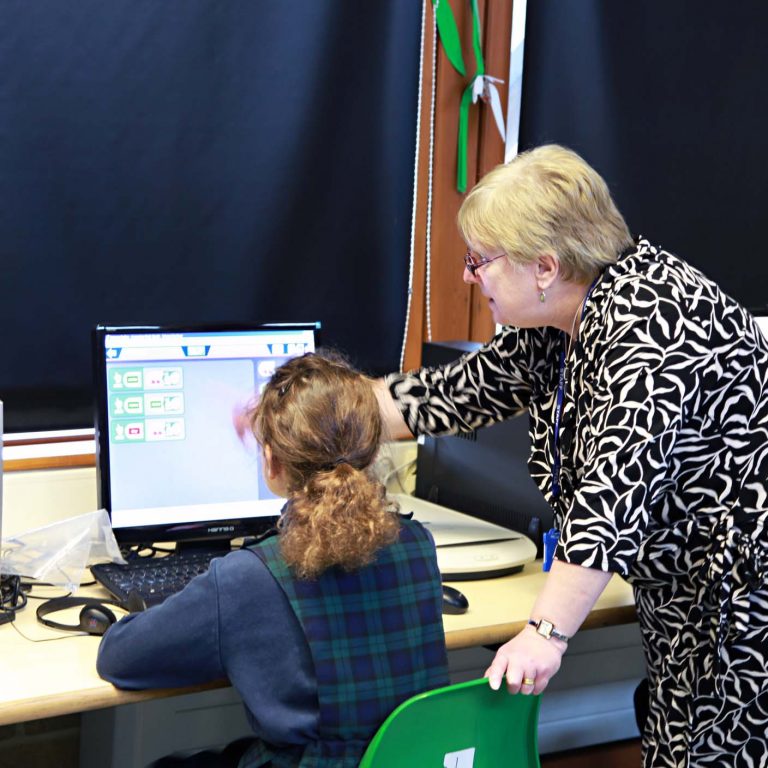 child looking at PC with a teacher